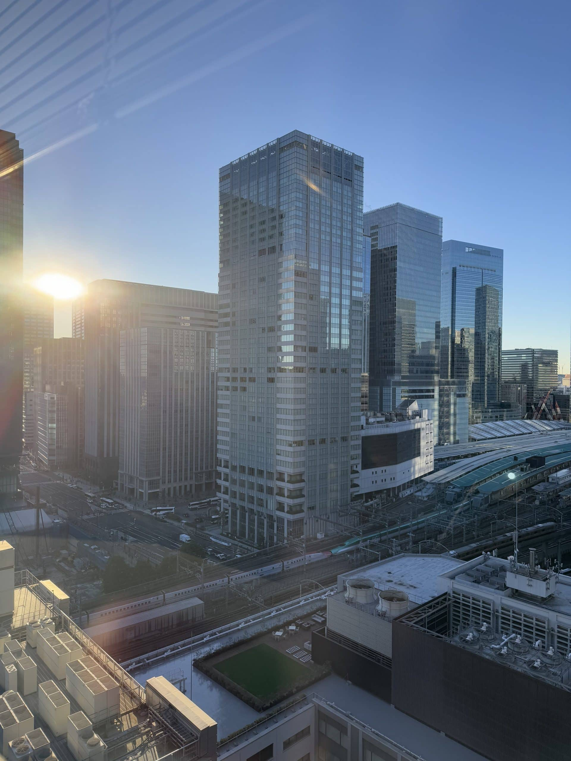 View from an 18th-floor window of my office, complete with sun flare and reflected window shutters. View is looking towards Tokyo Station and office buildings on the Yaesu side of the station. © 2025 Norbert Woehnl Photography.