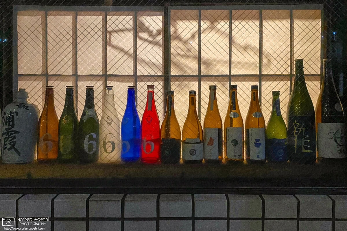 Emptied bottles of alcoholic drinks are lined up in a restaurant window in the Itabashi ward of Tokyo, Japan. © 2020 Norbert Woehnl Photography.
