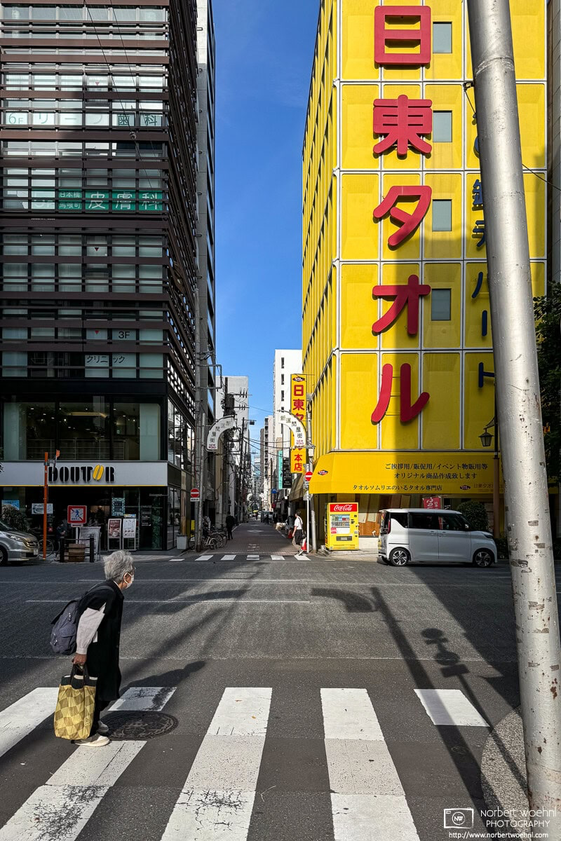 The strikingly yellow Nitto Towel Building in the Bakurocho area of Tokyo. An interesting area for street photography, it is worth to wait a few minutes and see what happens and who (or what) shows up as a potential photo subject. © 2024 Norbert Woehnl Photography.