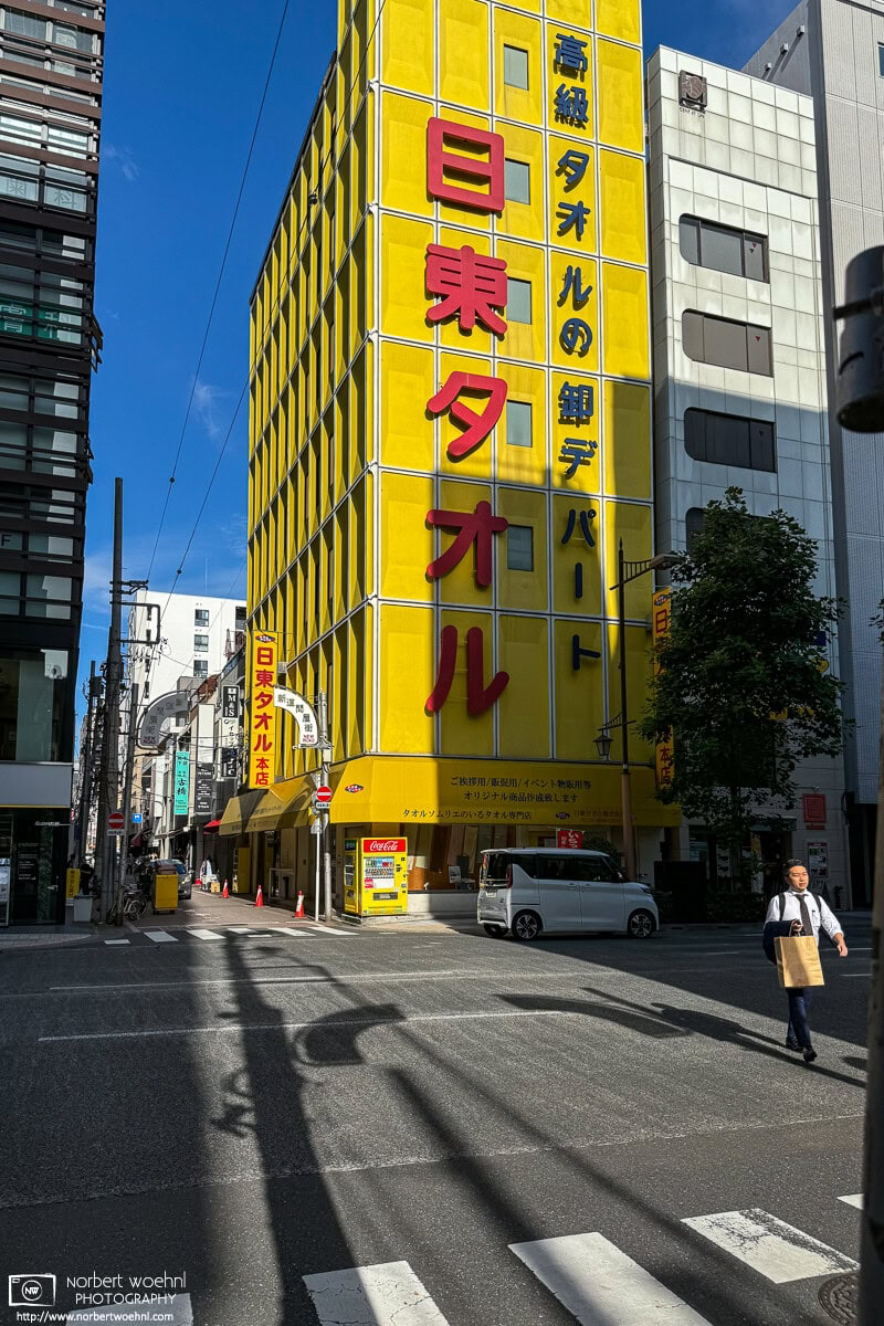 The strikingly yellow Nitto Towel Building in the Bakurocho area of Tokyo. An interesting area for street photography, it is worth to wait a few minutes and see what happens and who (or what) shows up as a potential photo subject. © 2024 Norbert Woehnl Photography.