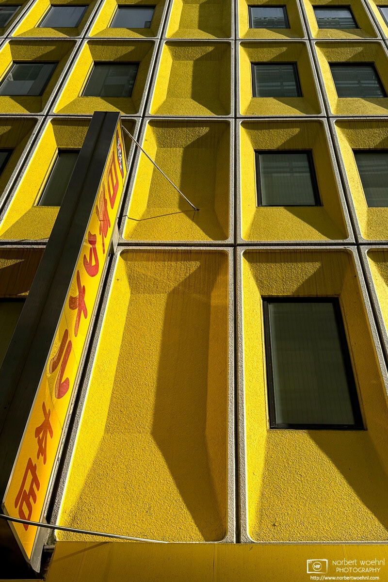 The strikingly yellow Nitto Towel Building in the Bakurocho area of Tokyo. An interesting area for street photography, it is worth to wait a few minutes and see what happens and who (or what) shows up as a potential photo subject. © 2024 Norbert Woehnl Photography.