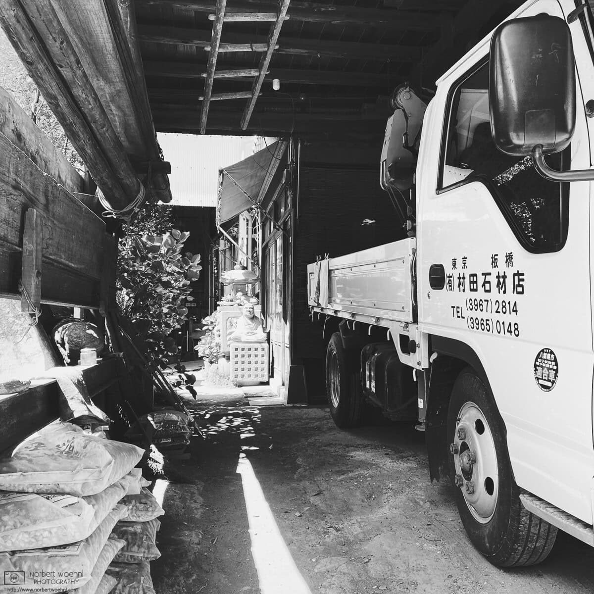 High-contrast monochrome photograph of a scene at Murata Stone Works, a small company making stone sculptures and other stone products in the Hasunuma-cho neighborhood of Itabashi Ward in Tokyo, Japan. © 2022 Norbert Woehnl Photography.
